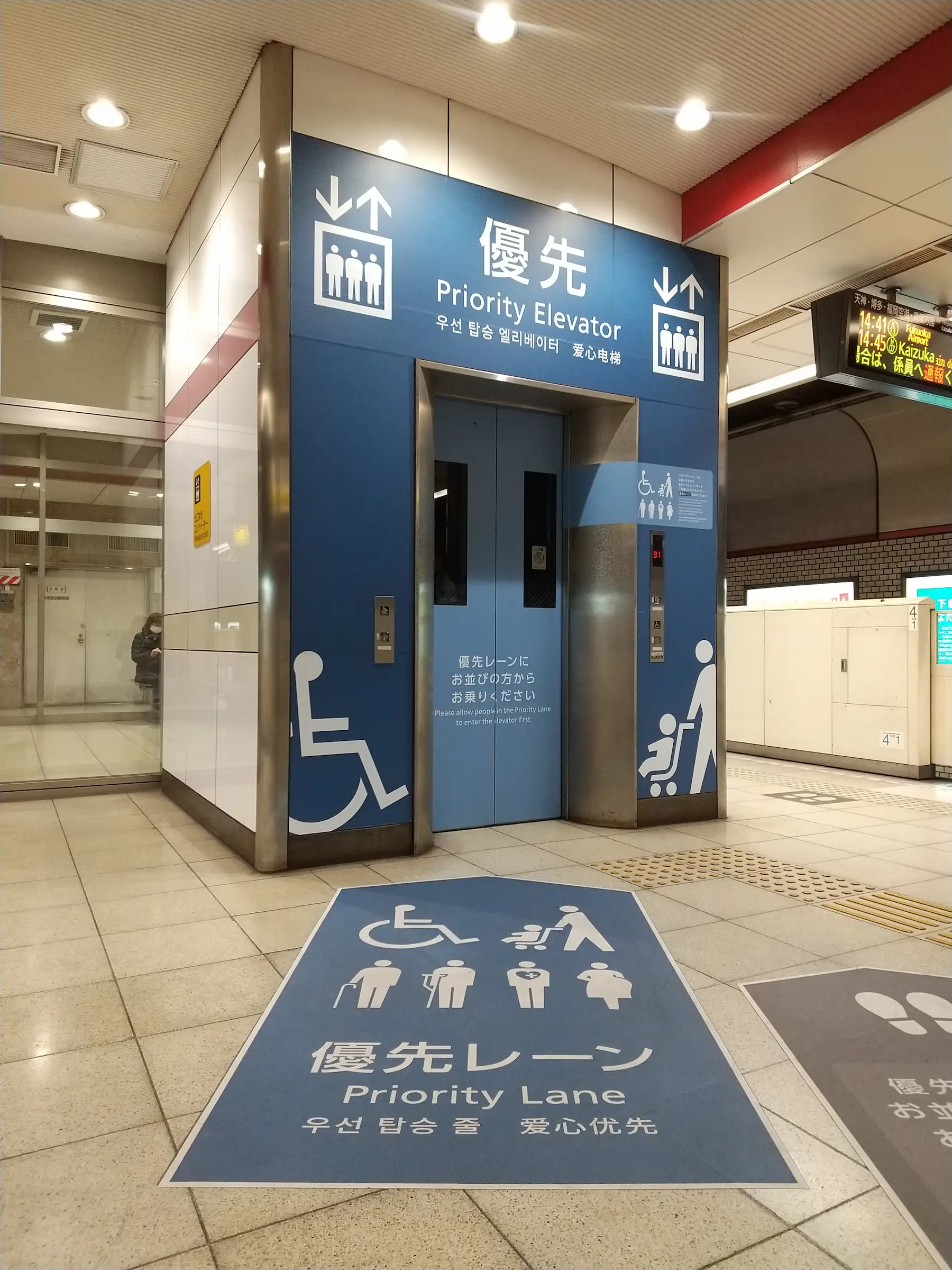 Ascenseur prioritaire en gare japonaise avec signalisation 優先レーン et pictogrammes poussette, fauteuil roulant, personne âgée