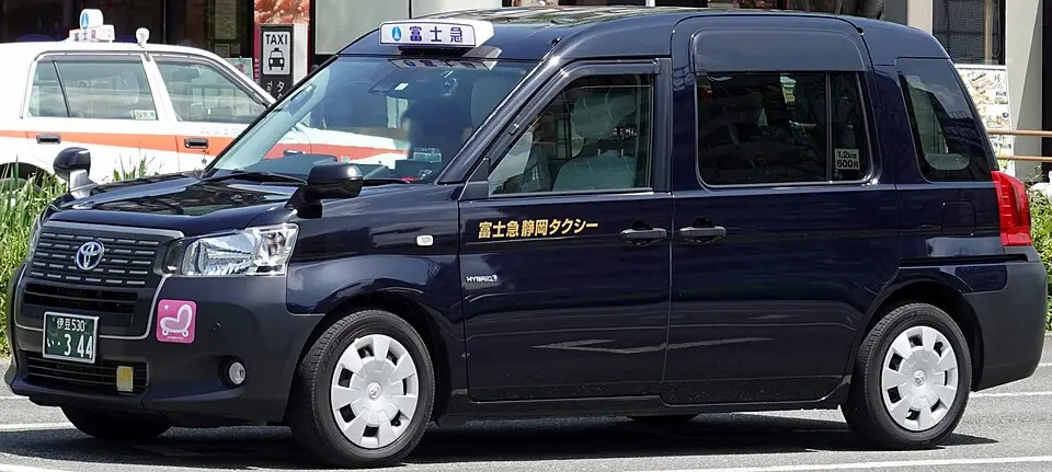 JPN Taxi noir Toyota avec porte coulissante et pictogramme bébé sur la carrosserie