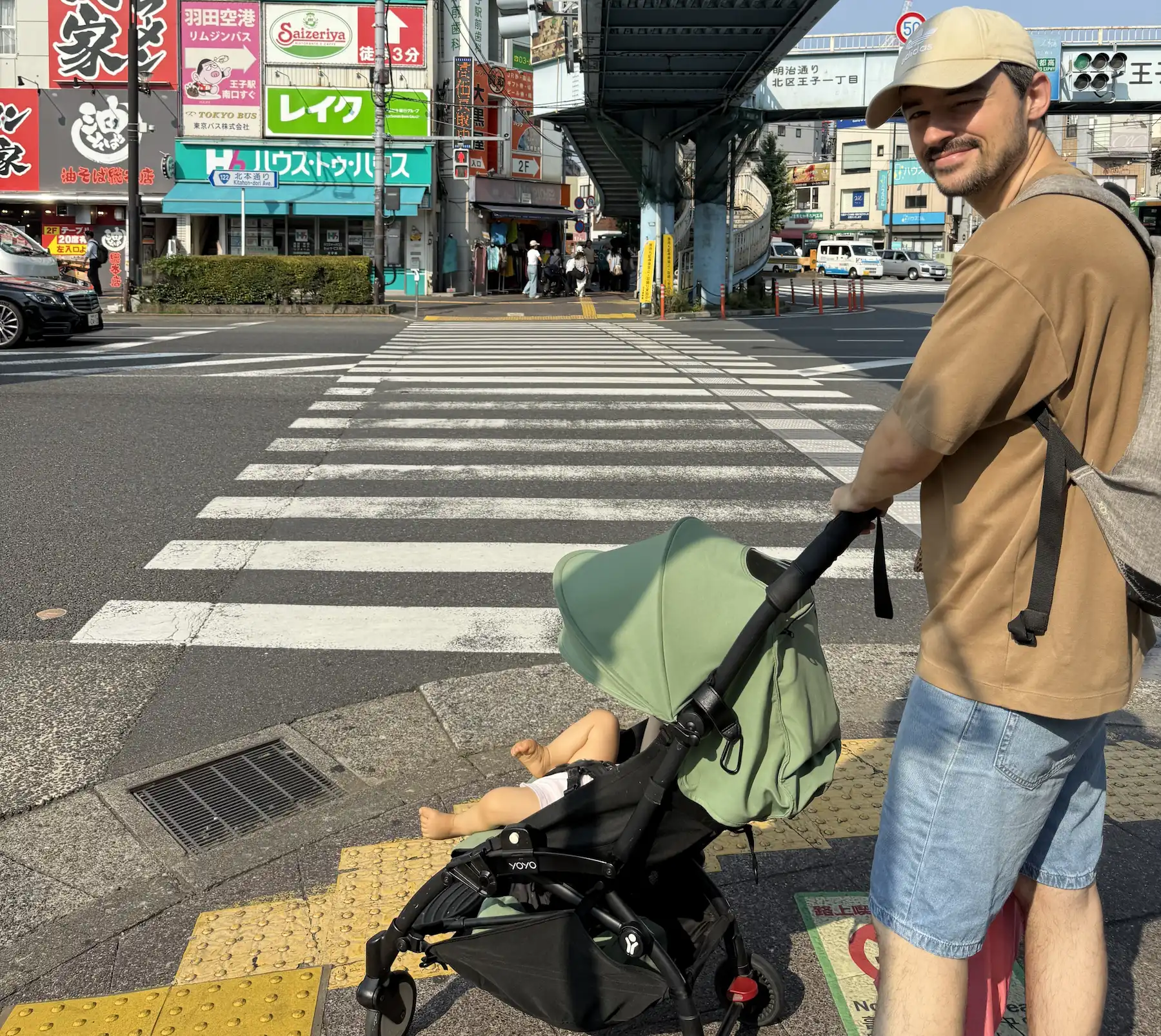Papa pousse une Yoyo verte au passage piéton de Tokyo, enseignes japonaises en arrière-plan