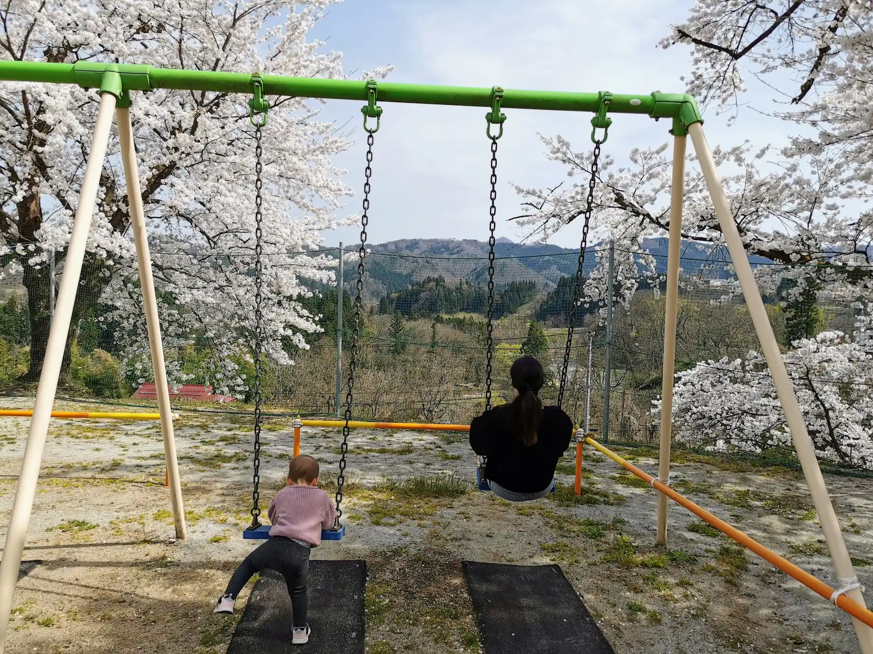 Mère et enfant sur les balançoires de l'école de montagne Yamagata, vue sur les cerisiers et les montagnes