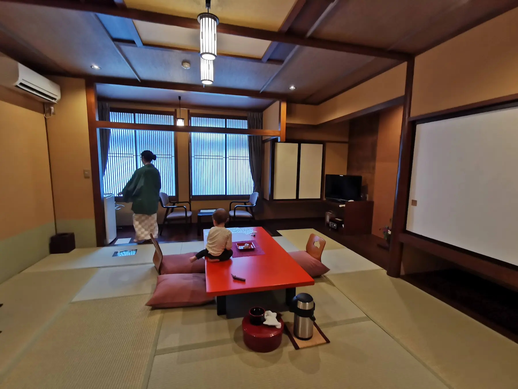 Chambre traditionnelle en tatami au ryokan Saikatei Jidaiya à Yamagata, table basse laquée rouge, zabuton et enfant assis