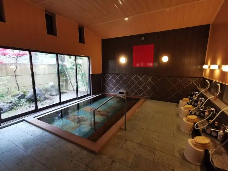 Bain thermal intérieur commun du ryokan Saikatei Jidaiya à Yamagata, bassin carrelé avec rampe, baie vitrée sur jardin et postes de douche avec tabourets en bois