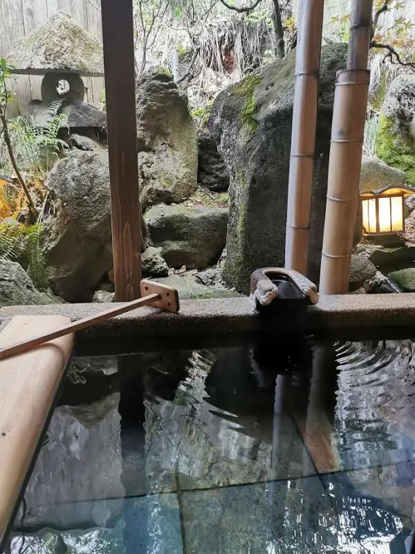 Onsen privatif extérieur du ryokan Saikatei Jidaiya à Yamagata, bassin d'eau thermale entouré de rochers moussus, tiges de bambou et lanterne en pierre