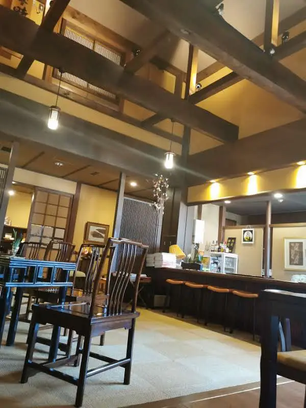 Grand salon du ryokan Saikatei Jidaiya à Yamagata, plafond double hauteur à poutres apparentes, chaises en bois sombre et comptoir de bar
