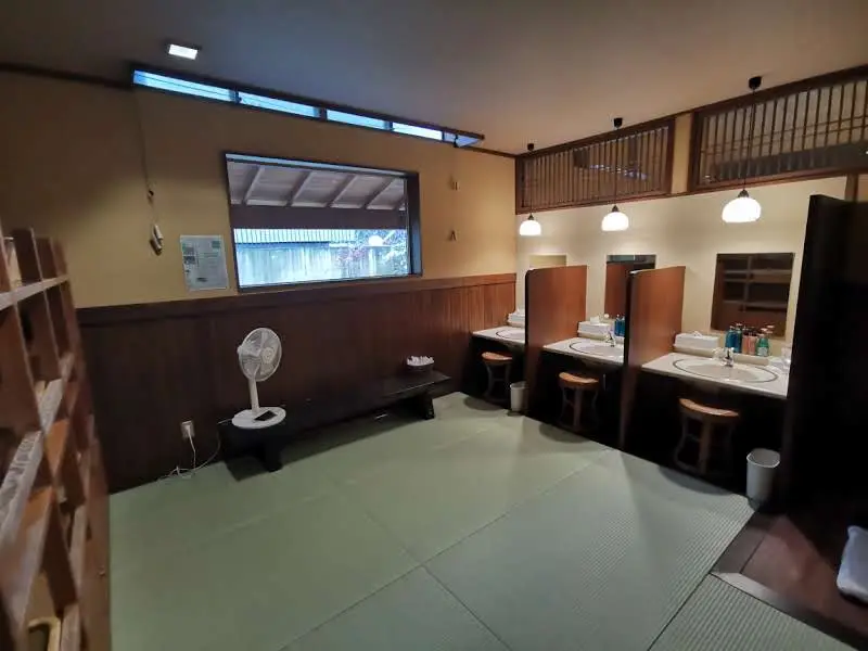 Vestiaire de l'onsen du ryokan Saikatei Jidaiya à Yamagata, sol en tatami, coiffeuses individuelles avec miroirs et produits de soin, étagères à paniers