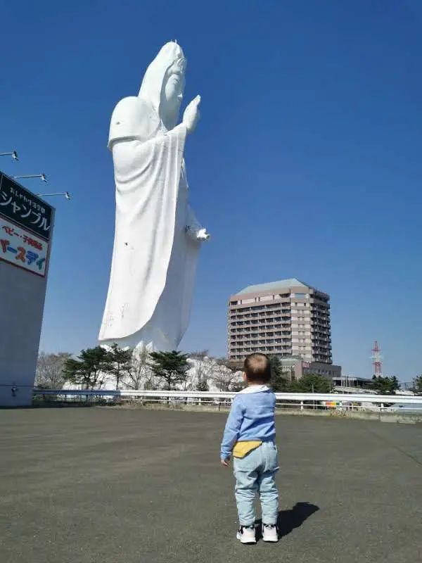 Enfant face à la statue géante blanche du Sendai Daikannon sous un ciel bleu